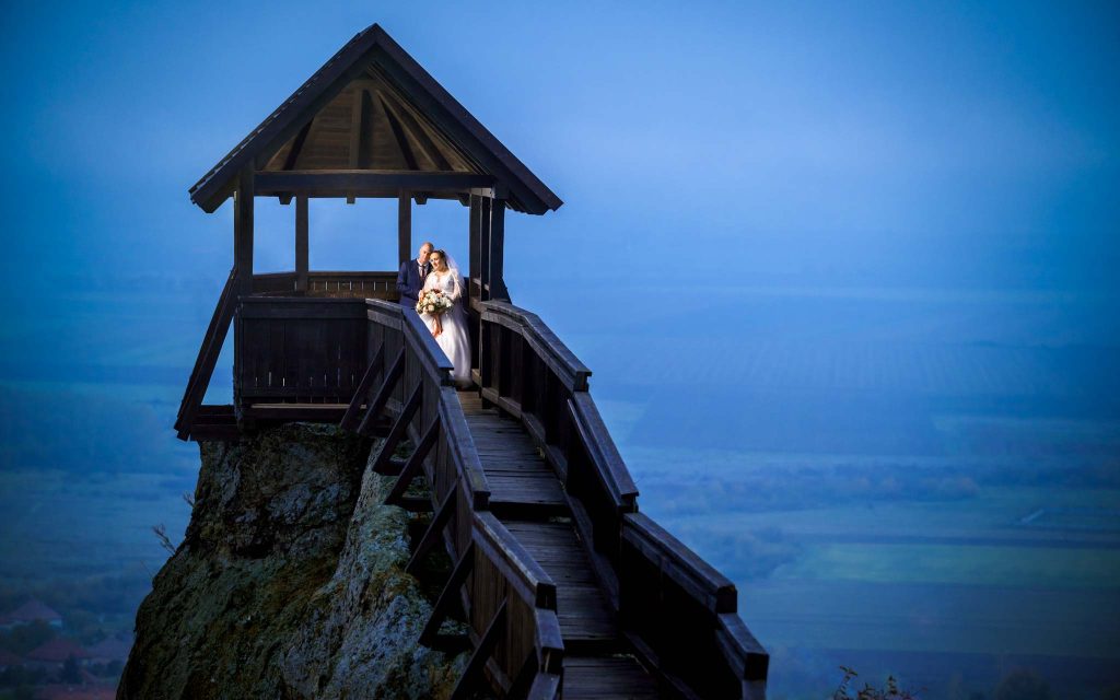 Boldogkő vára bástyáján áll a házaspár kékszínű ködben. Esküvői fotós Debrecen